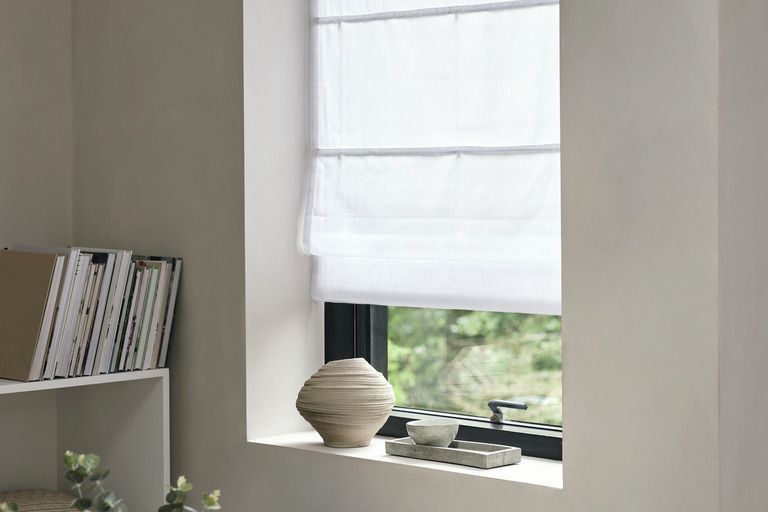 White roman blind in a recessed window with ceramics on the sill