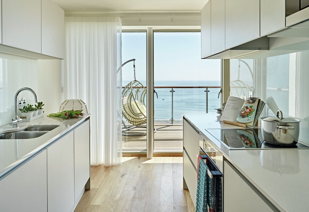 Galley kitchen with sheer curtains framing the sea and balcony