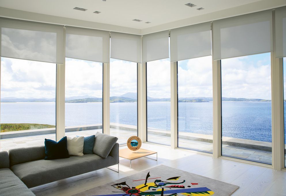 Corner living room with roller blinds on wrap-around glazing overlooking the sea